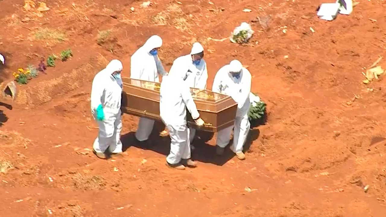 Agentes funerários com roupas de proteção carregando urna