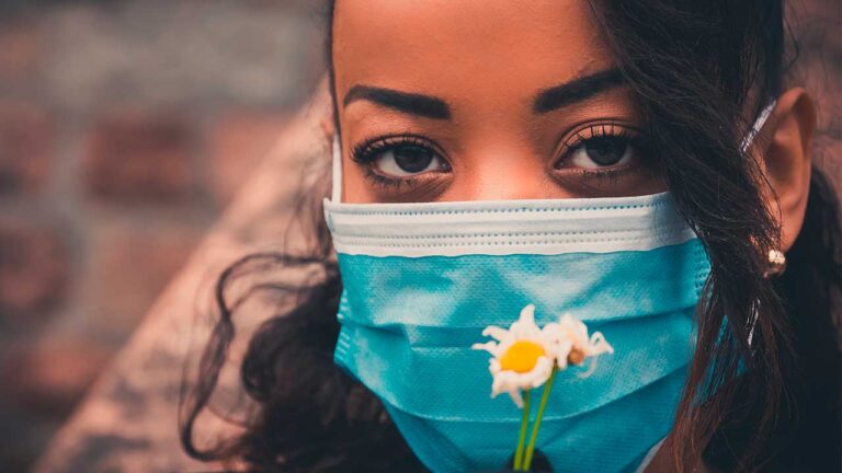 Mulher segurando flor com máscara em sinal de esperança