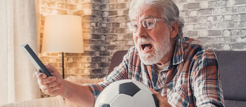 Homem idoso assistindo ao jogo com bola de futebol ao lado
