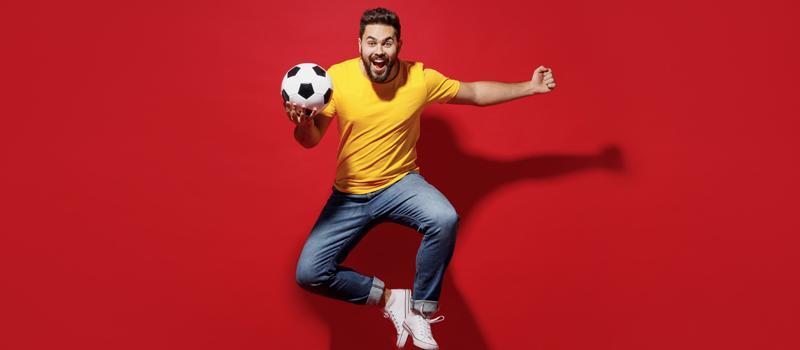 Homem num fundo vermelho pulando com bola de futebol na mão